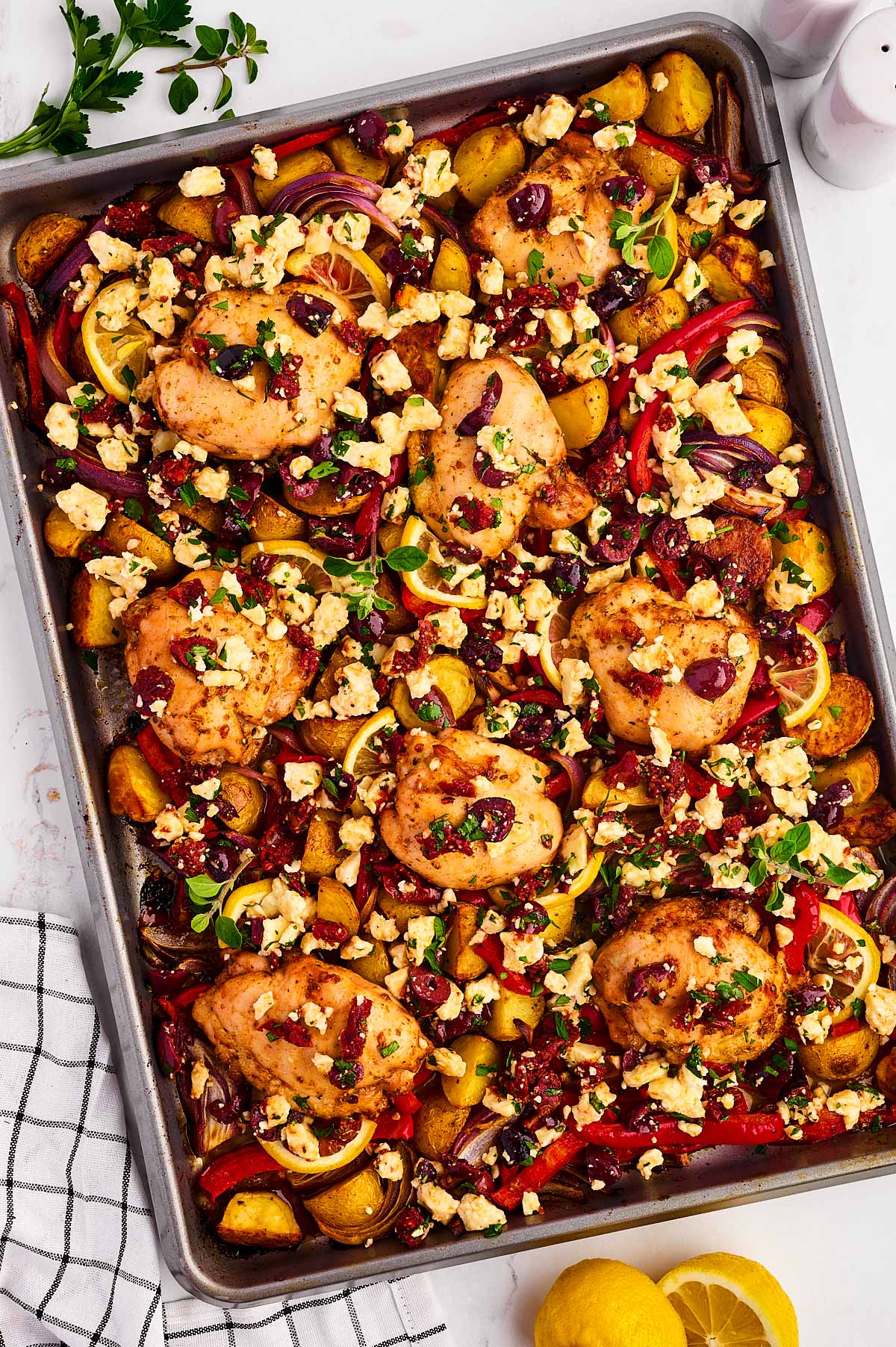 overhead view of greek chicken on sheet pan with vegetables and olives