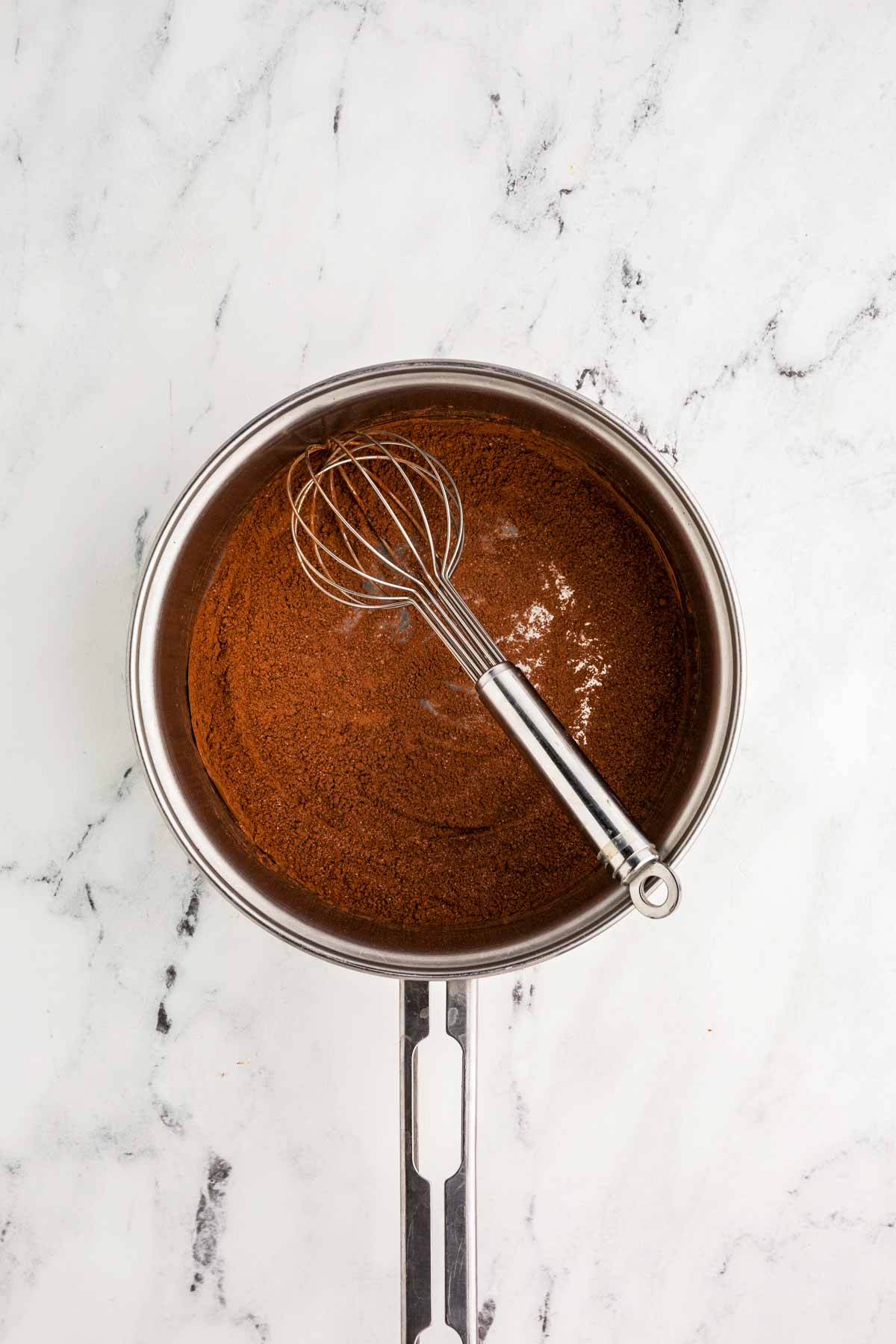 overhead view of sugar and cocoa powder in saucepan with whisk