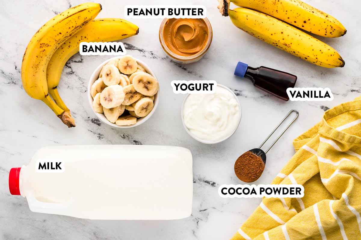 overhead view of ingredients to make a chocolate peanut butter banana smoothie with text labels