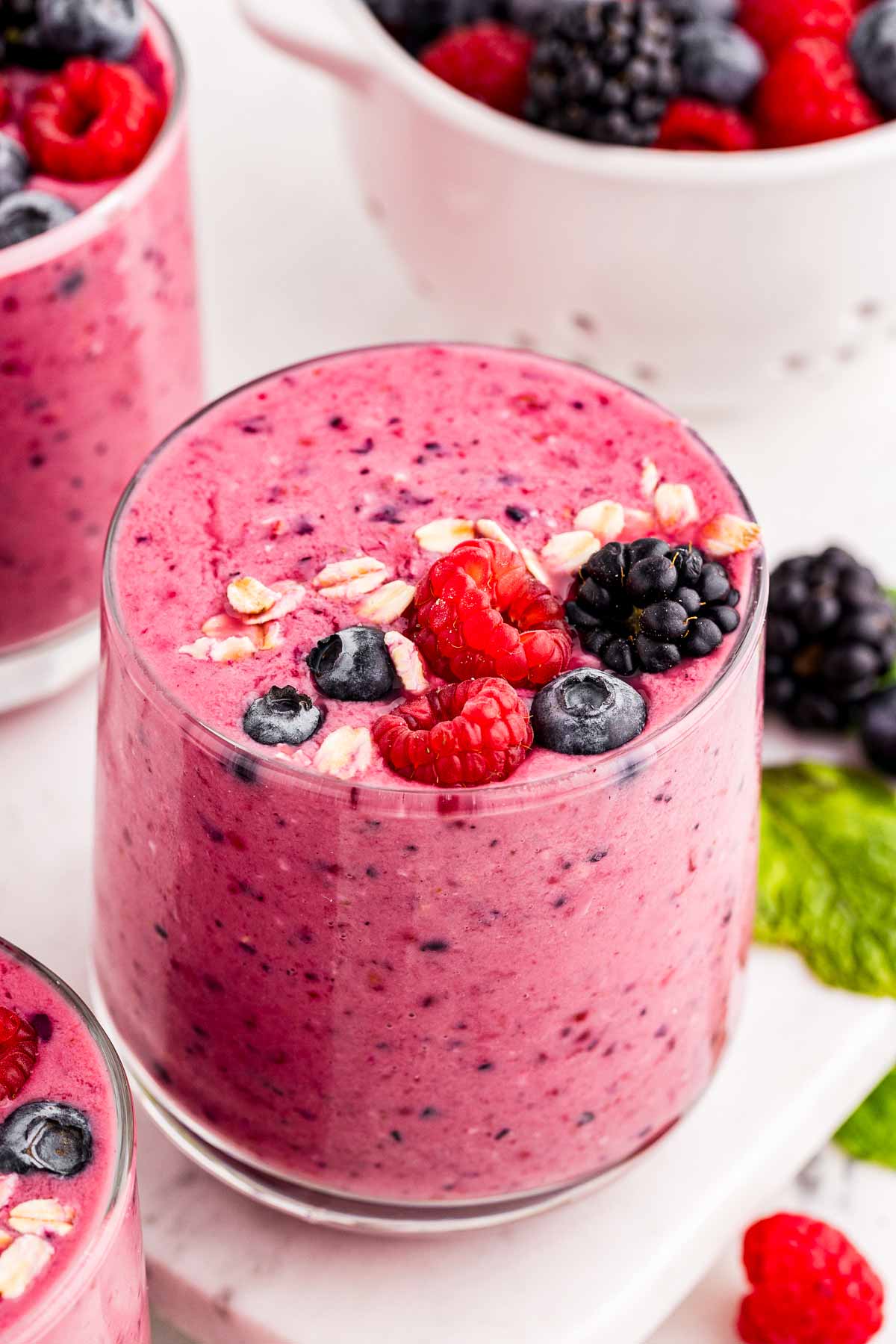 frontal view of berry smoothie in glass surrounded by more smoothies and berries