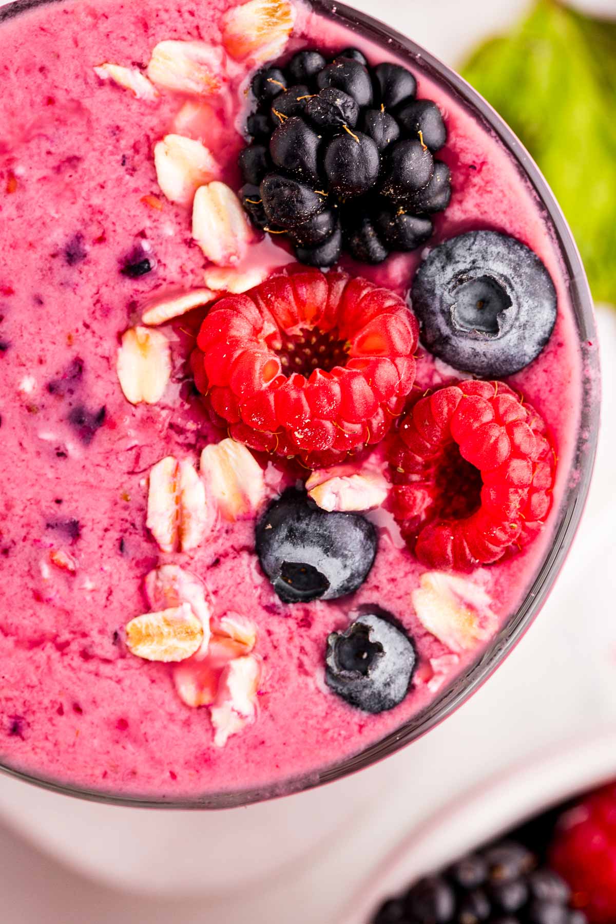 overhead close up view of mixed berry smoothie in glass topped with fresh berries, oats and chia seeds