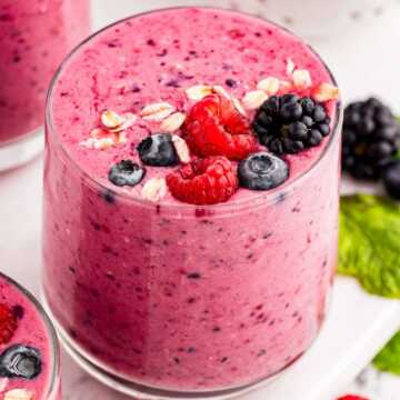 frontal view of berry smoothie in glass surrounded by more smoothies and berries