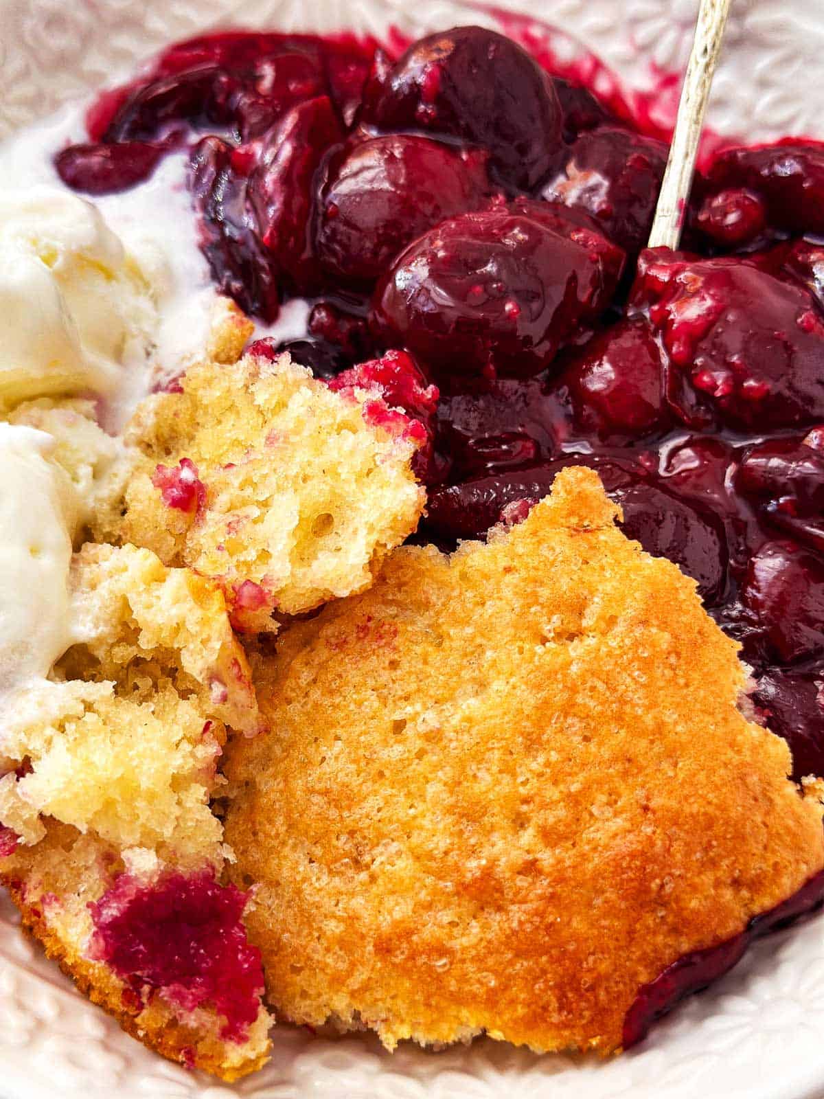 close up photo of cherry cobbler with vanilla ice cream in white bowl