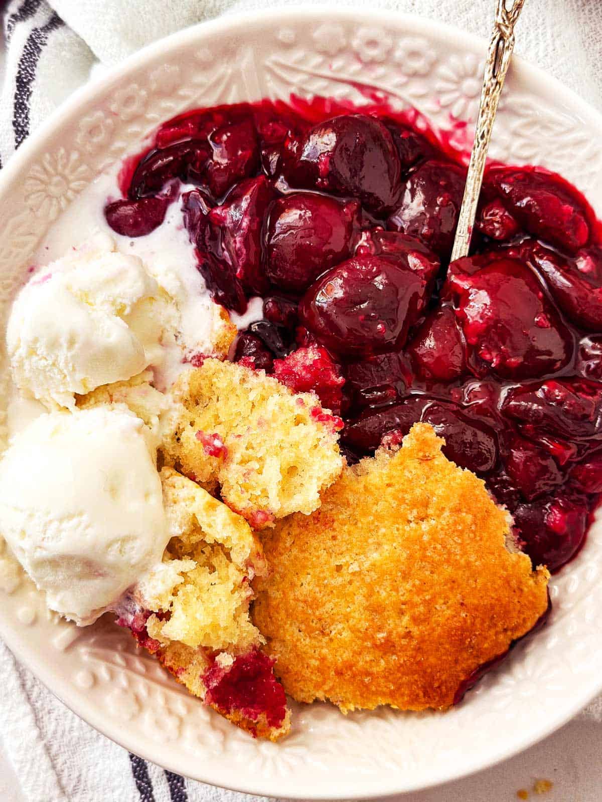 overhead view of cherry cobbler in white bowl with ice cream