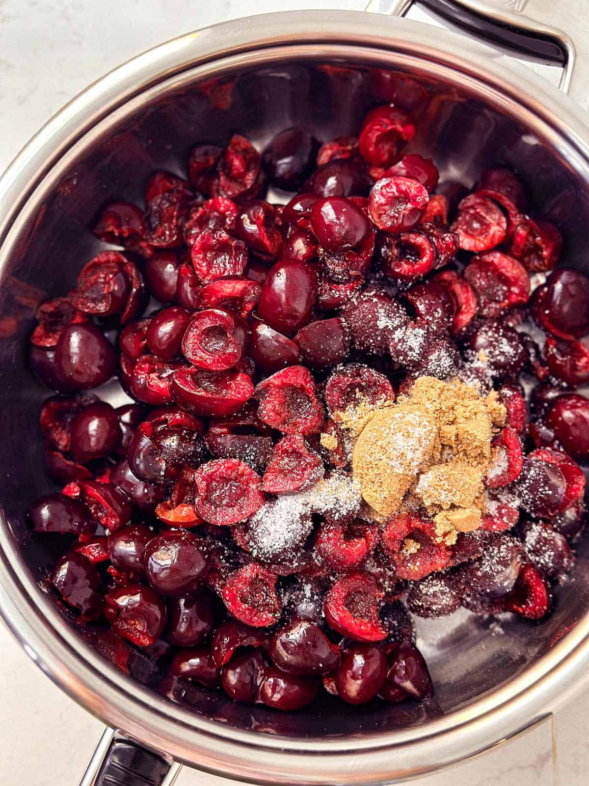 overhead view of fresh pitted cherries and sugar in pan