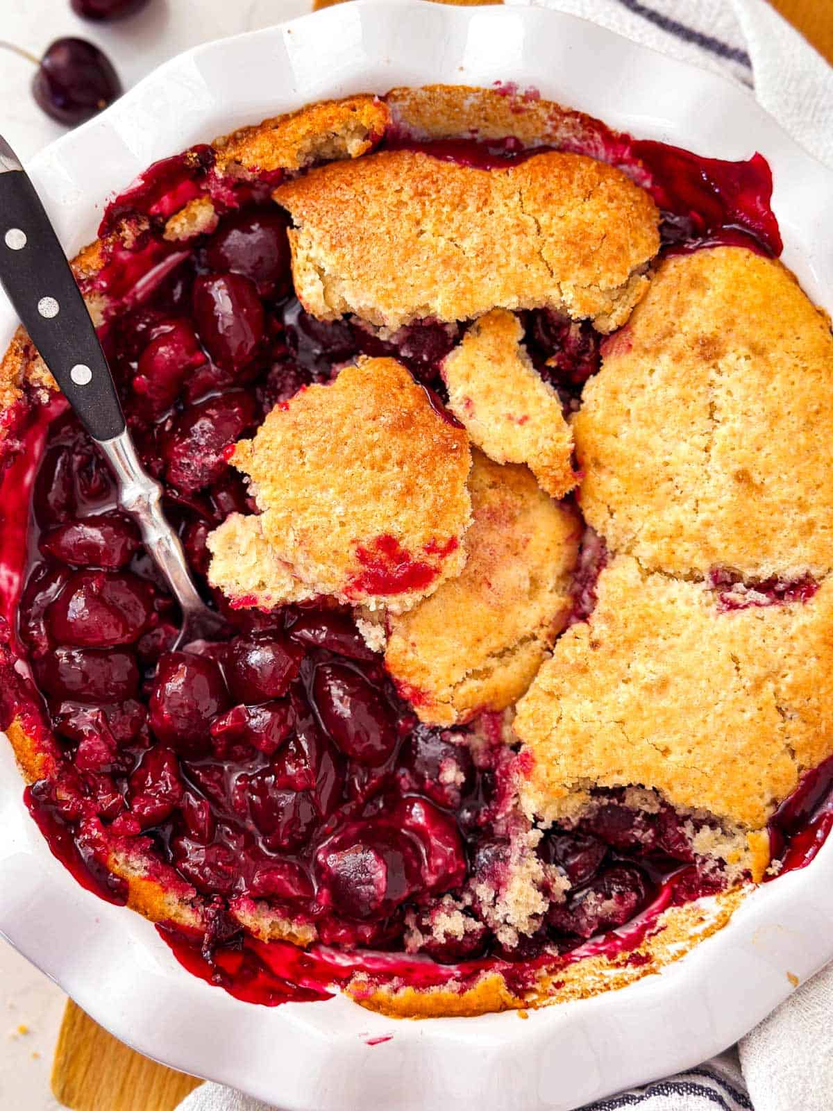 overhead view of baked cherry cobbler with spoon stuck in