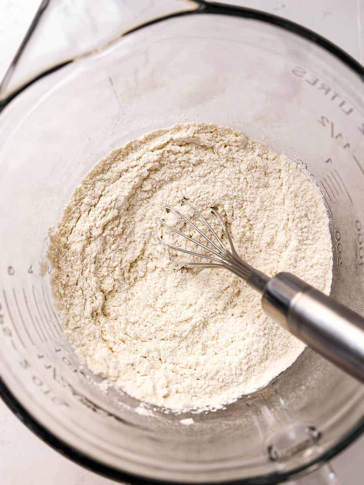 overhead view of flour in glass bowl with whisk