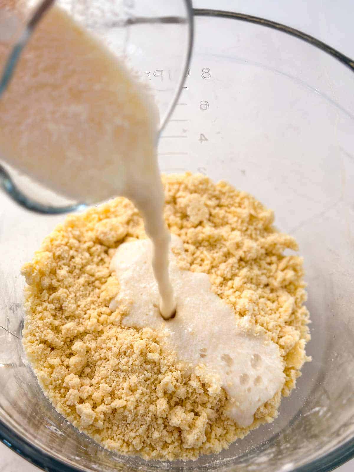 buttermilk pouring over flour and butter mixture in glass bowl