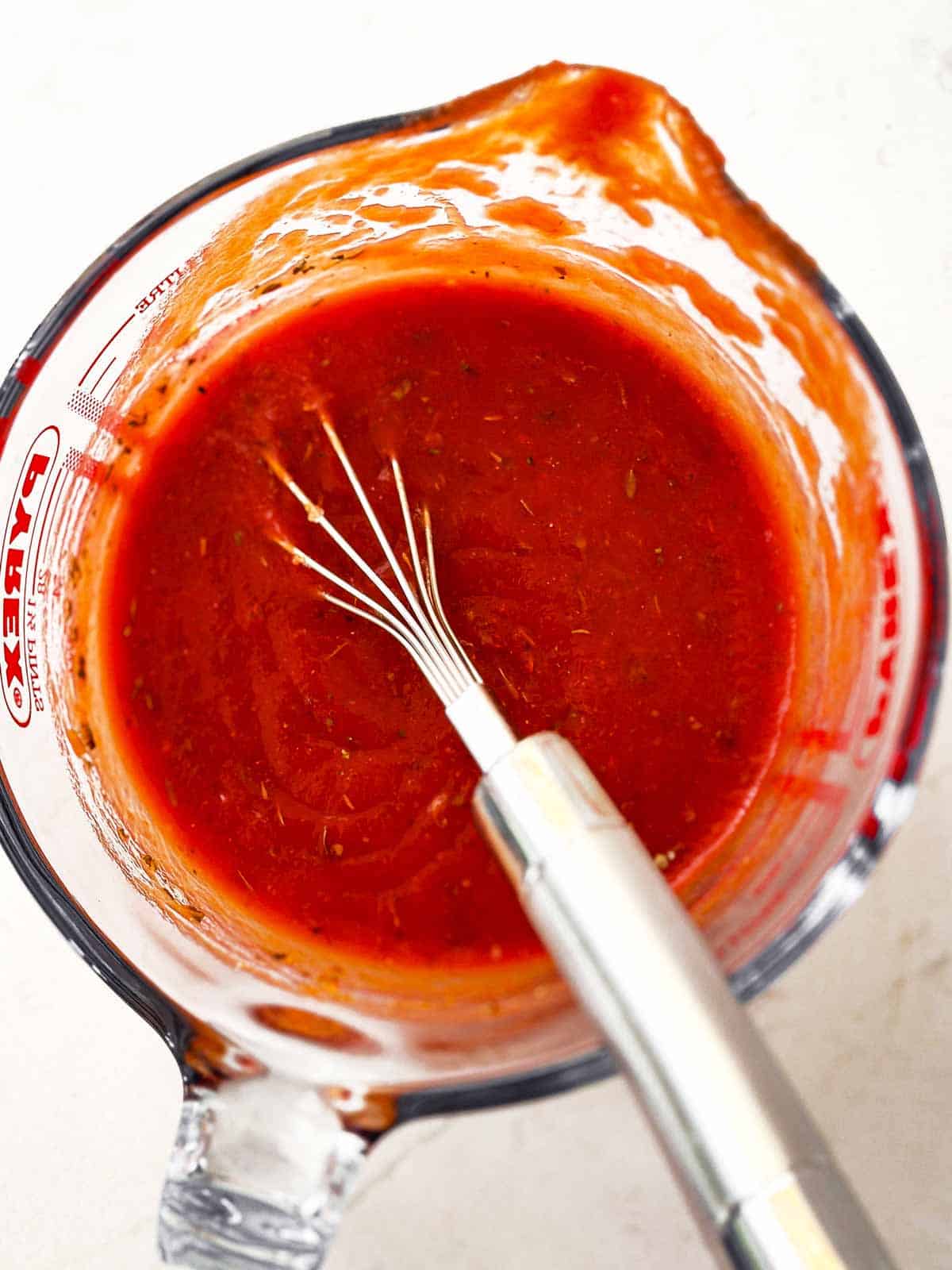 tomato sauce in measuring jug with whisk