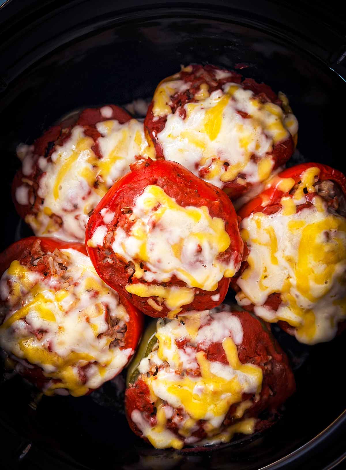 overhead view of cooked stuffed peppers topped with cheese in crockpot