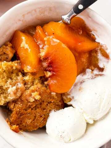 overhead close up view of peach cobbler in white bowl