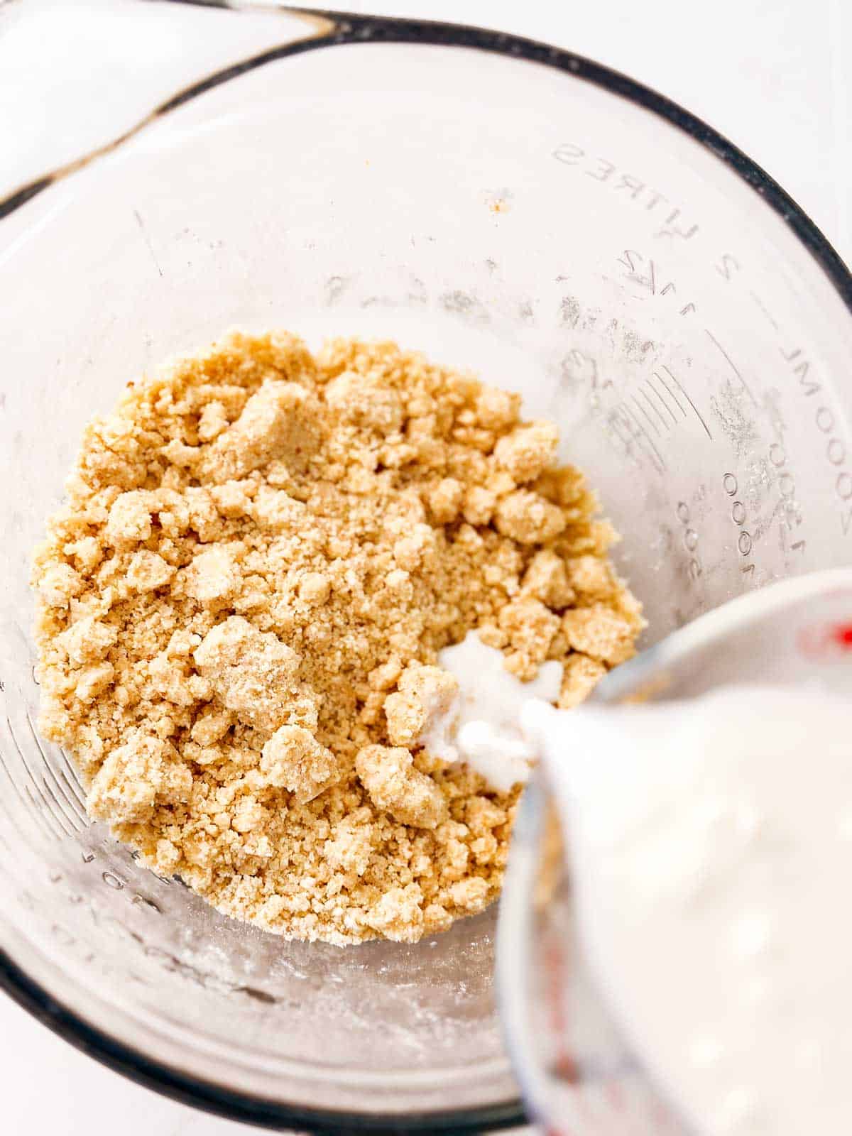 overhead view of buttermilk pouring over crumb mixture in glass bowl