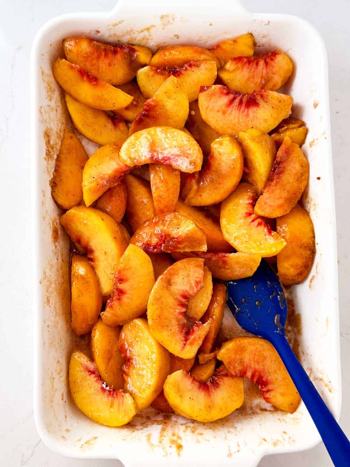 overhead view of uncooked peach slices in white casserole dish