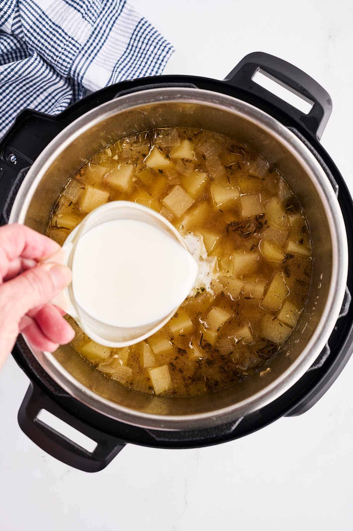 female hand pouring cornstarch slurry from glass measuring jug into potato soup in instant pot