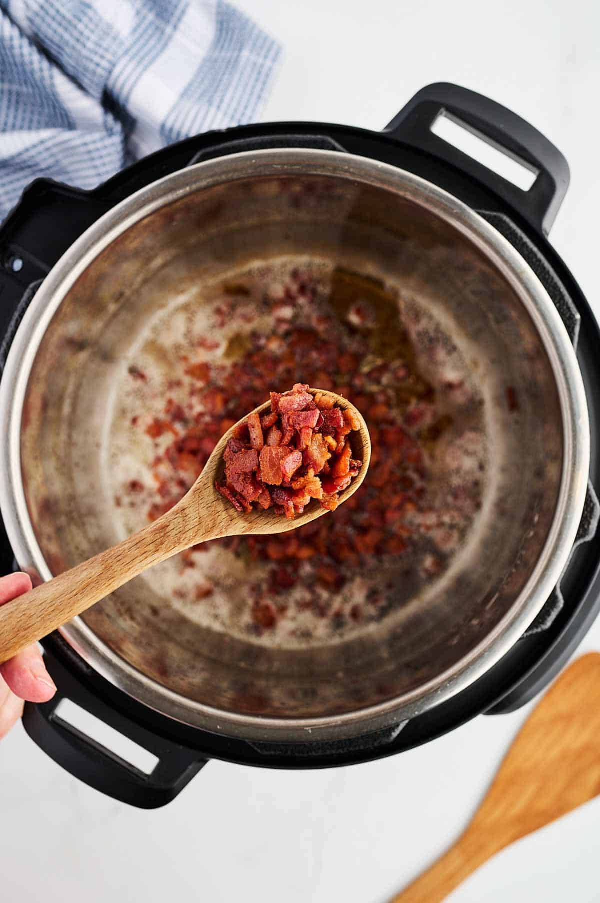 overhead view of cooked chopped bacon in wooden spoon over instant pot