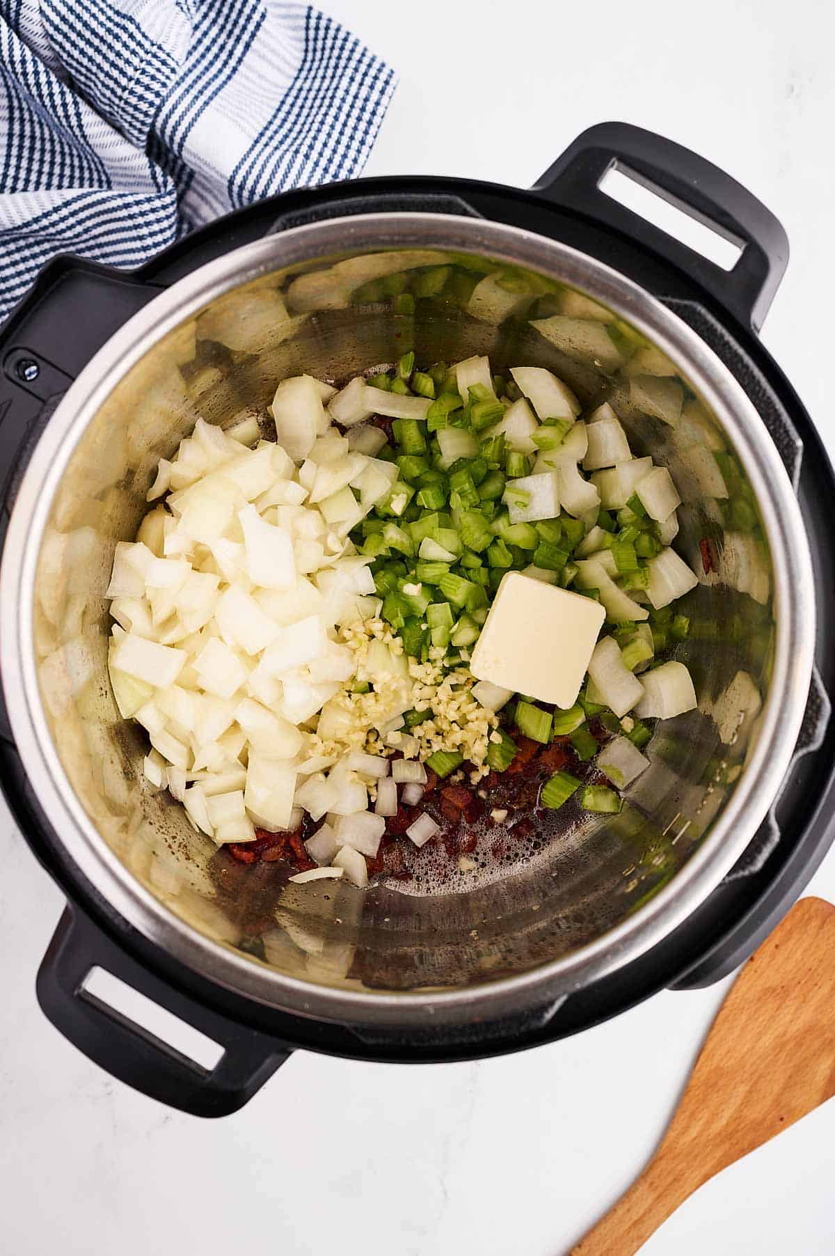 overhead view of uncooked aromatic vegetables and butter in instant pot