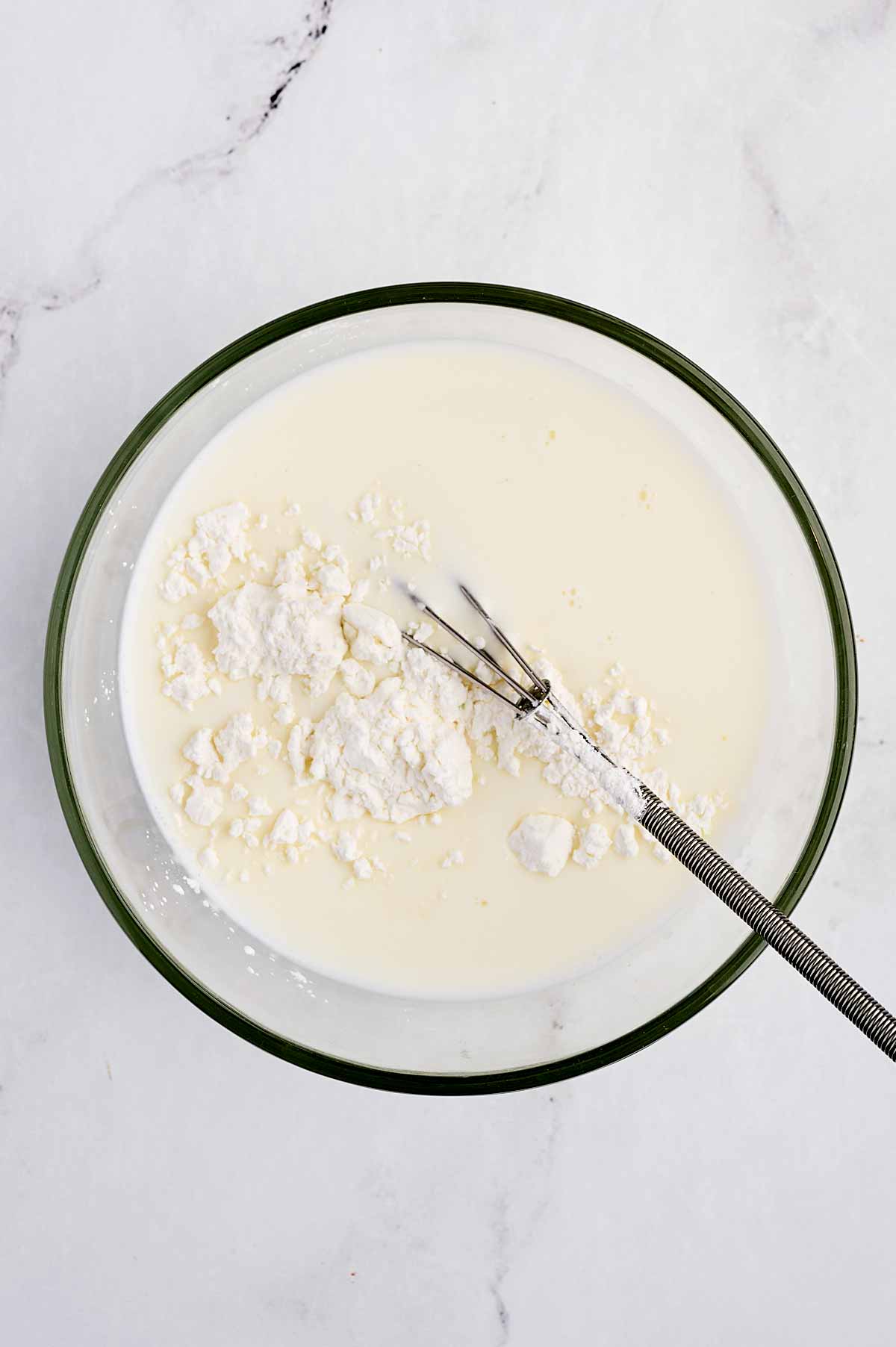 overhead view of cornstarch in milk in glass bowl with whisk