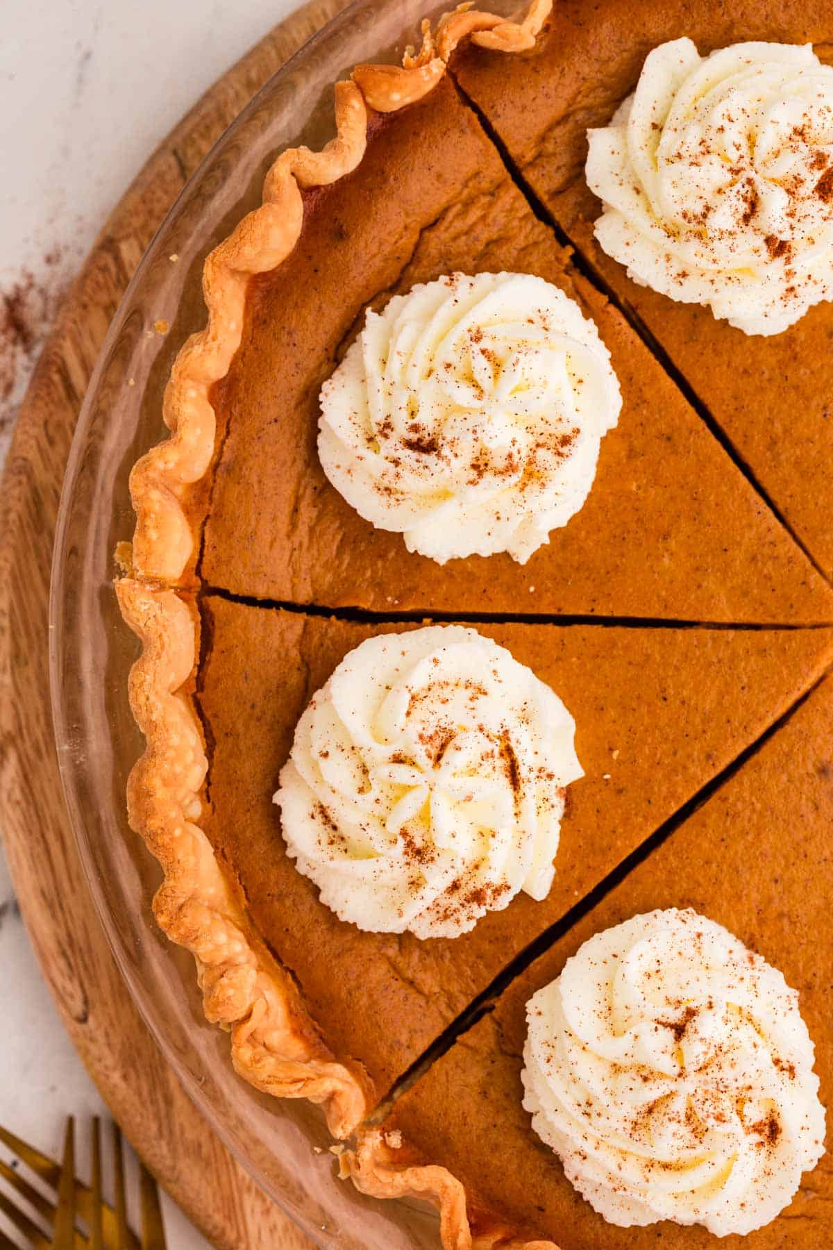 overhead close up view of sliced pumpkin pie garnished with whipped cream