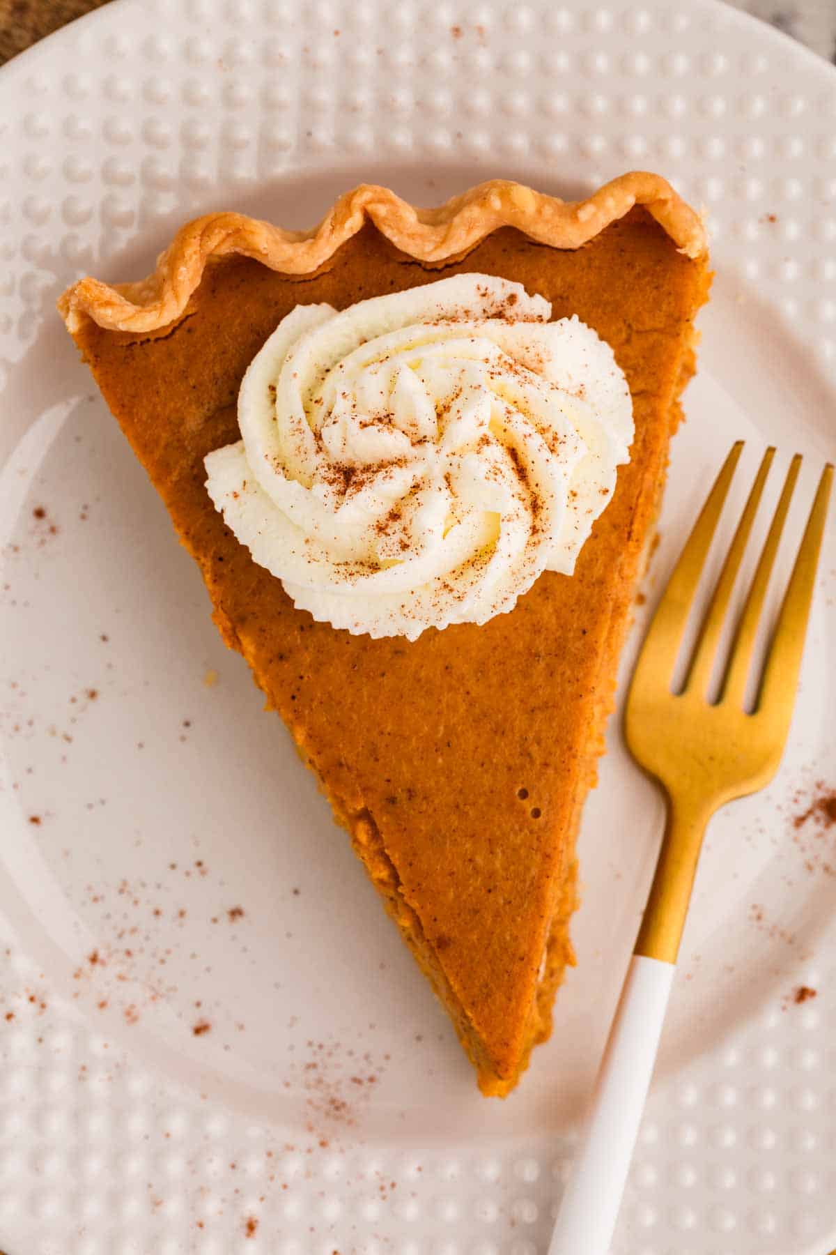 overhead view of pumpkin pie slice on white plate with golden fork