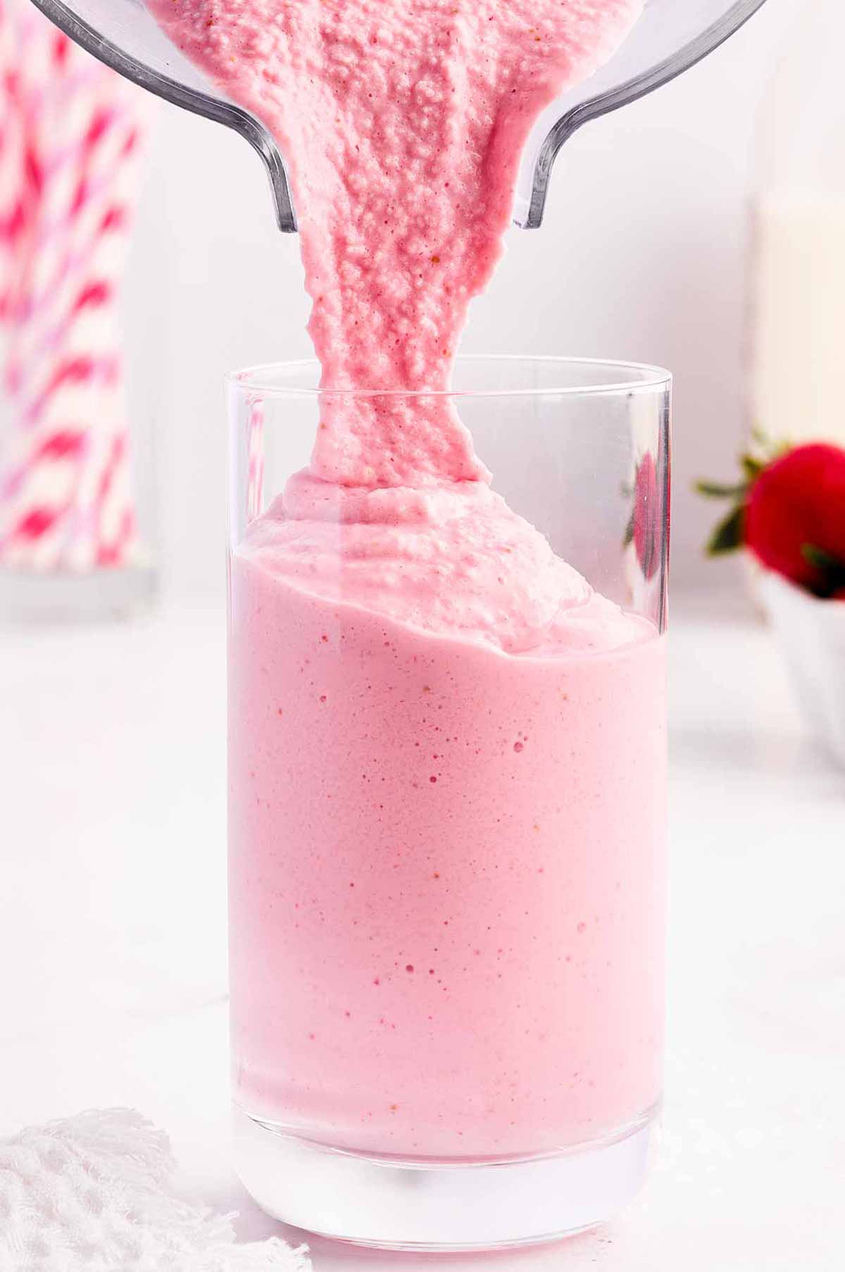 strawberry yogurt smoothie pouring into glass from blender cup