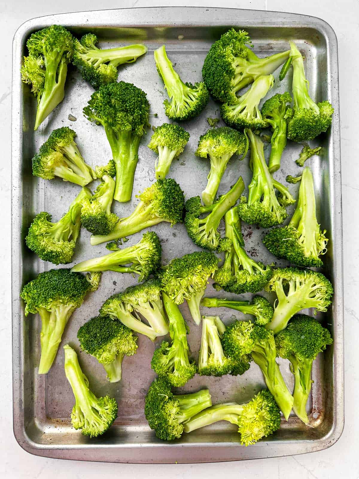 overhead view of sheet pan filled with raw broccoli florets