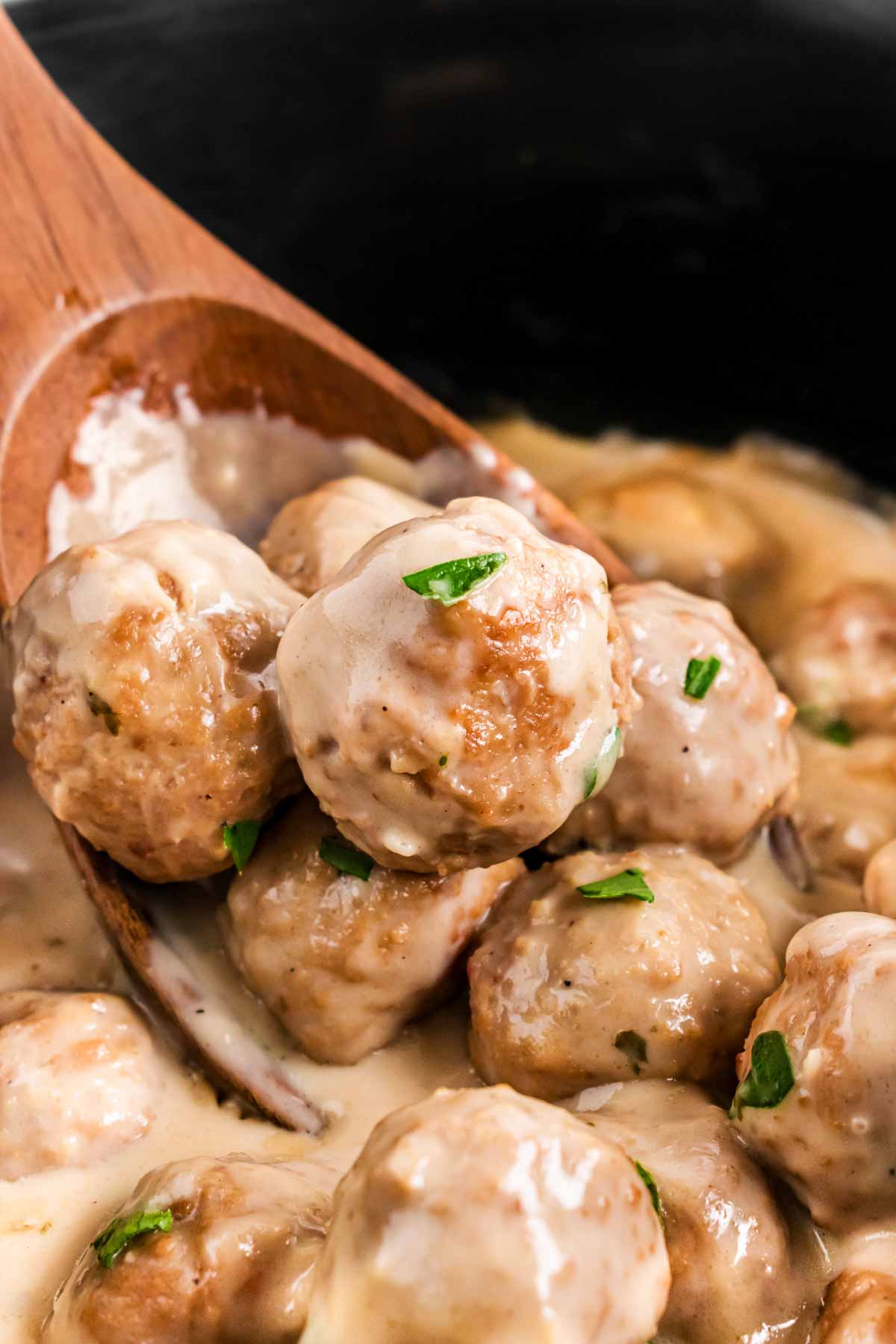 close up frontal view of wooden spoon in crock with Swedish meatballs