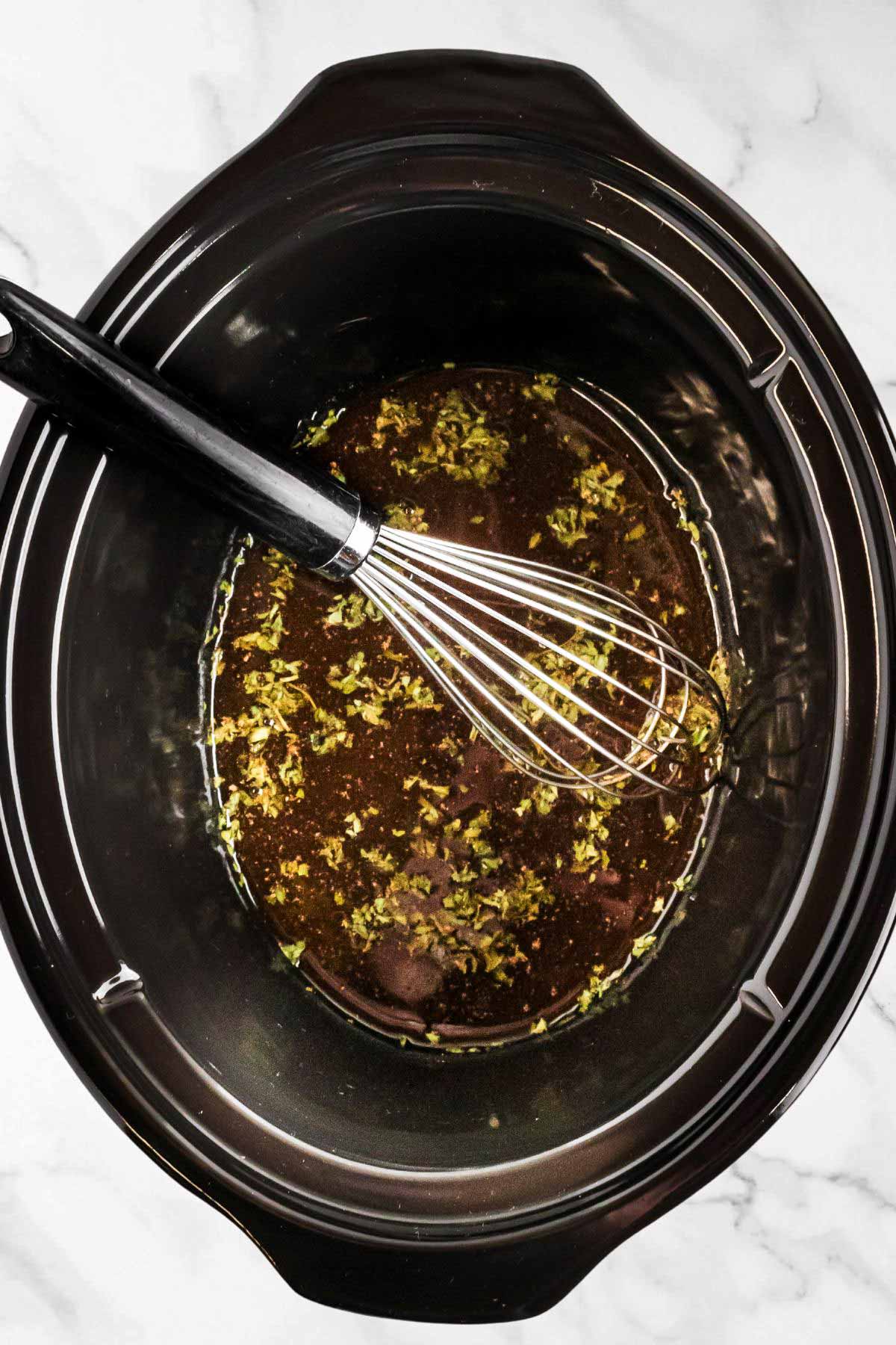 overhead view of black crock with broth and seasoning with whisk