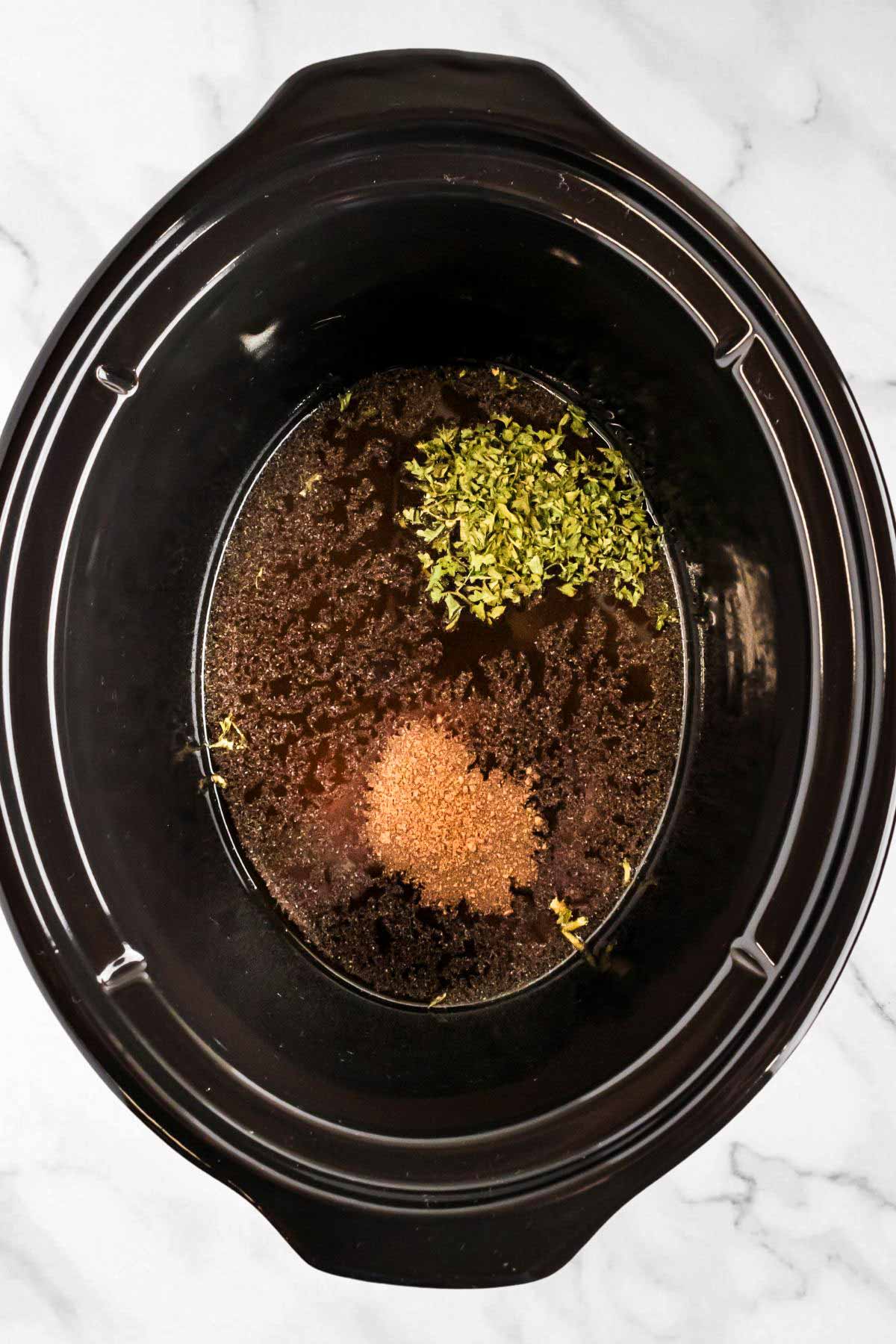 overhead view of seasoning on top of broth in slow cooker