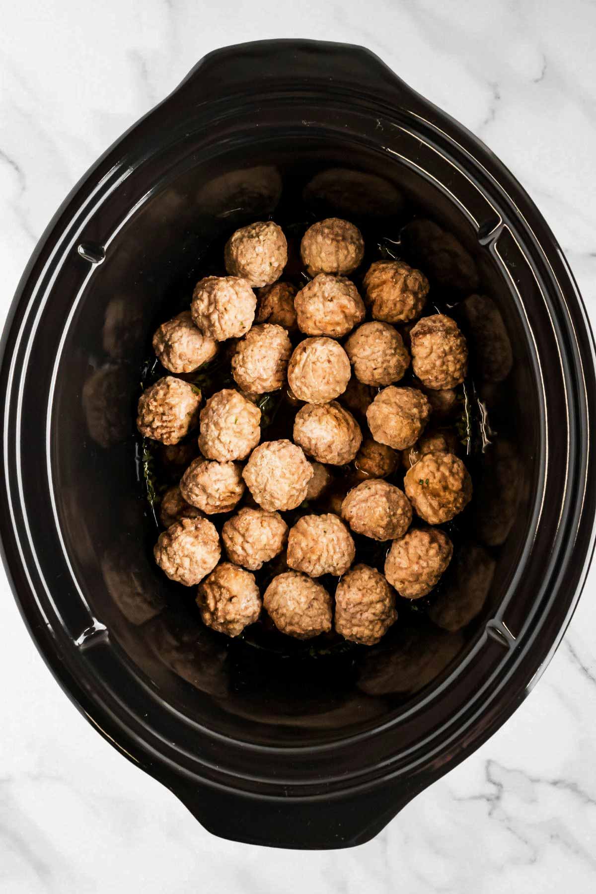 overhead view of meatballs in slow cooker with broth