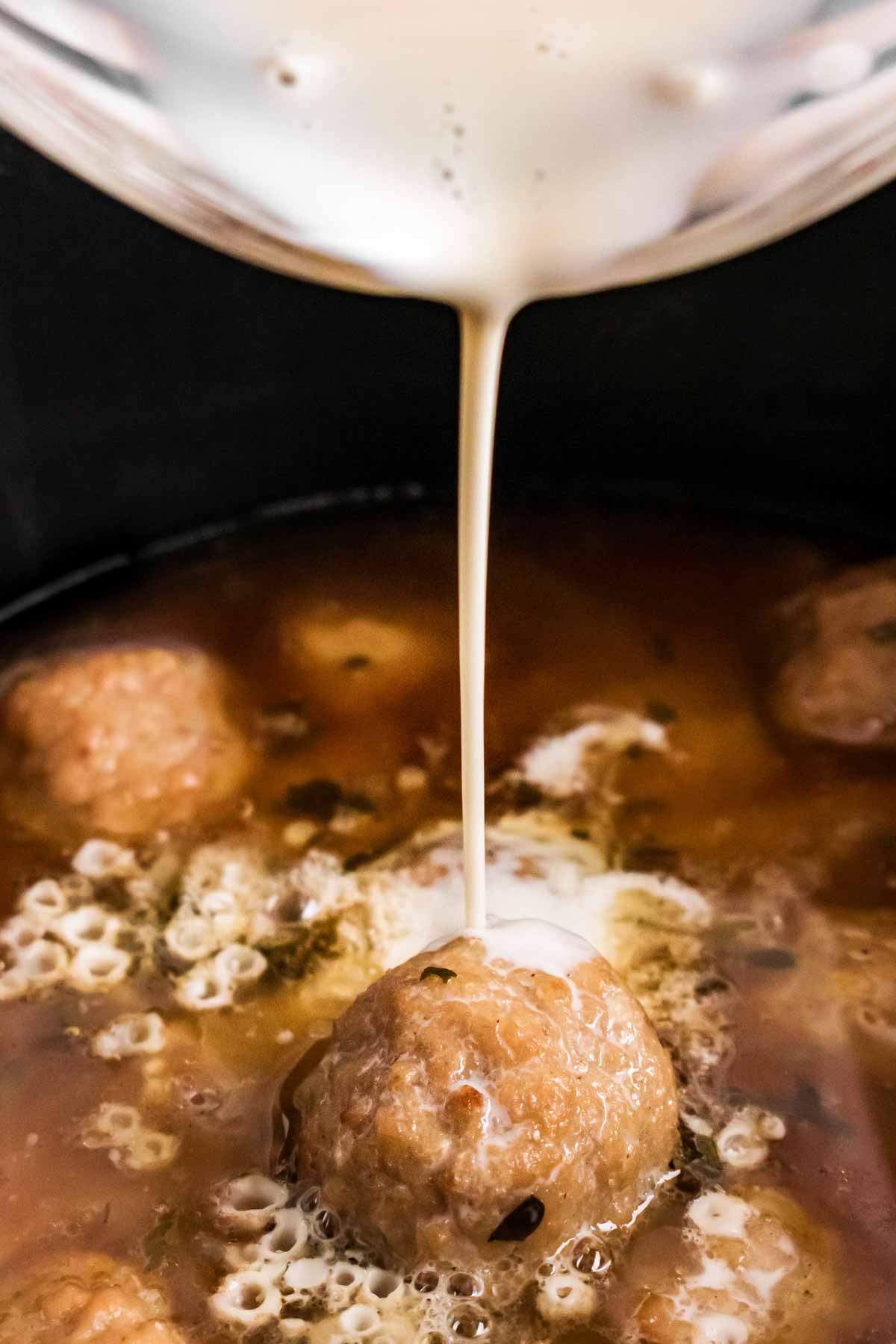 frontal view of cream drizzling over Swedish meatballs in black crock