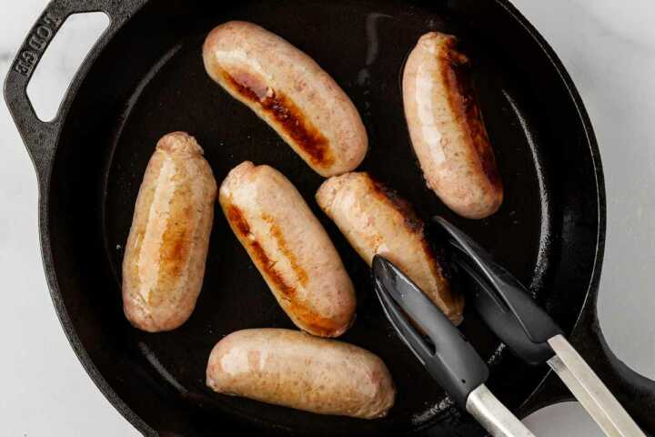 sausages being browned in cast iron skillet