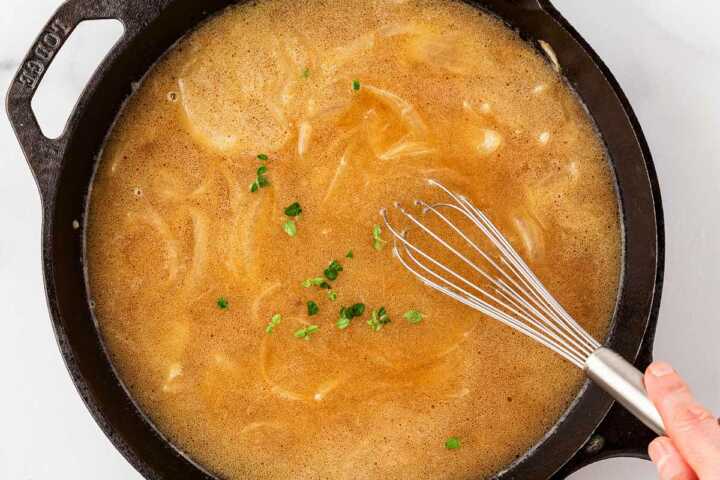 onion gravy being whisked in a cast iron skillet