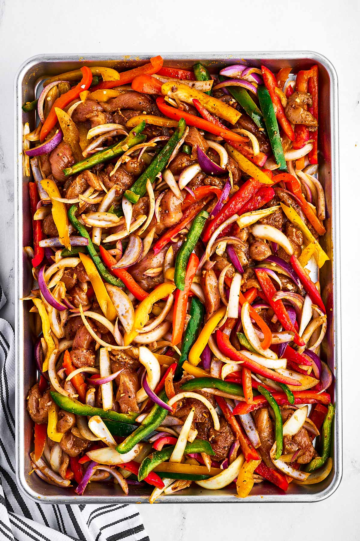 overhead view of uncooked chicken fajita mixture on sheet pan