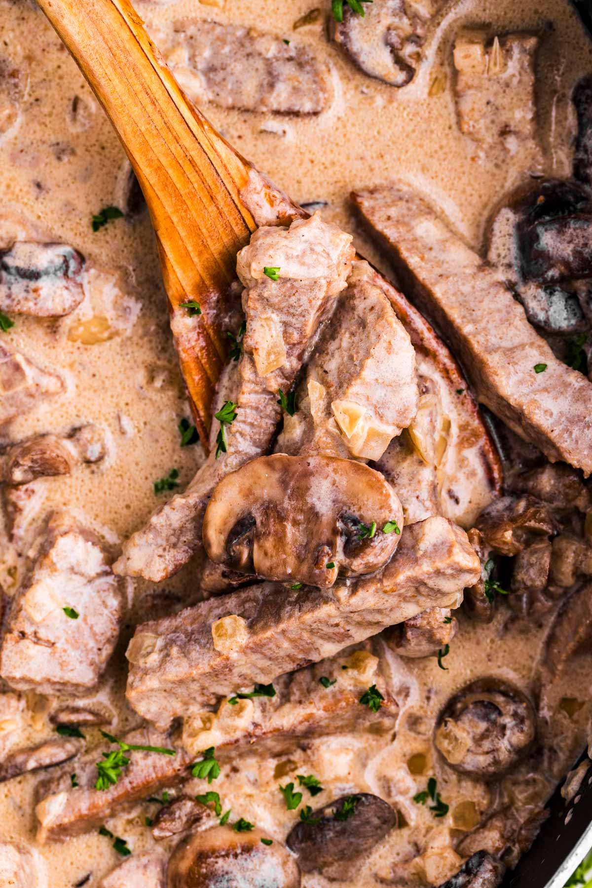 overhead close up view of beef stroganoff on wooden spoon in skillet