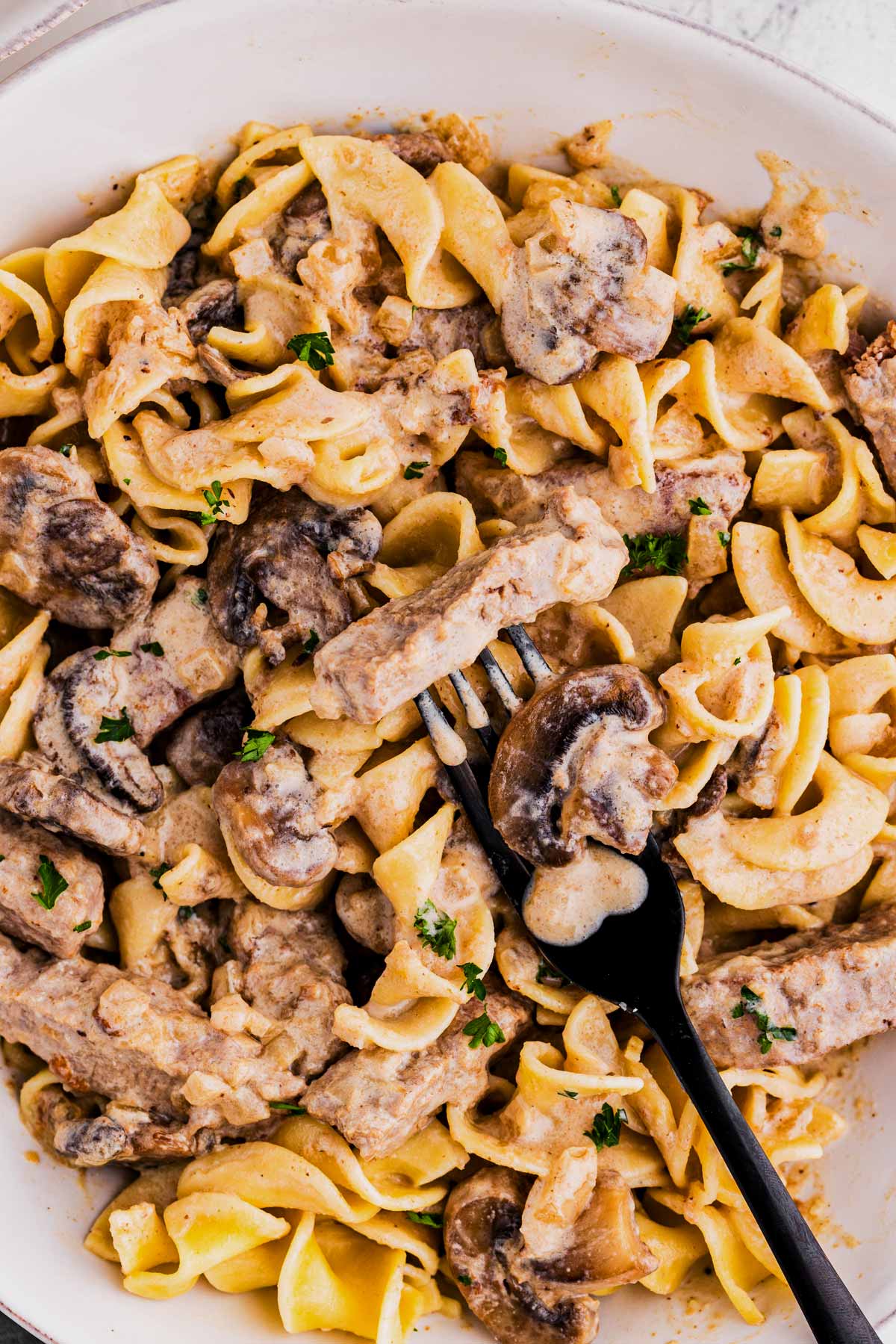 overhead close up of noodles wixed with beef stroganoff on white plate