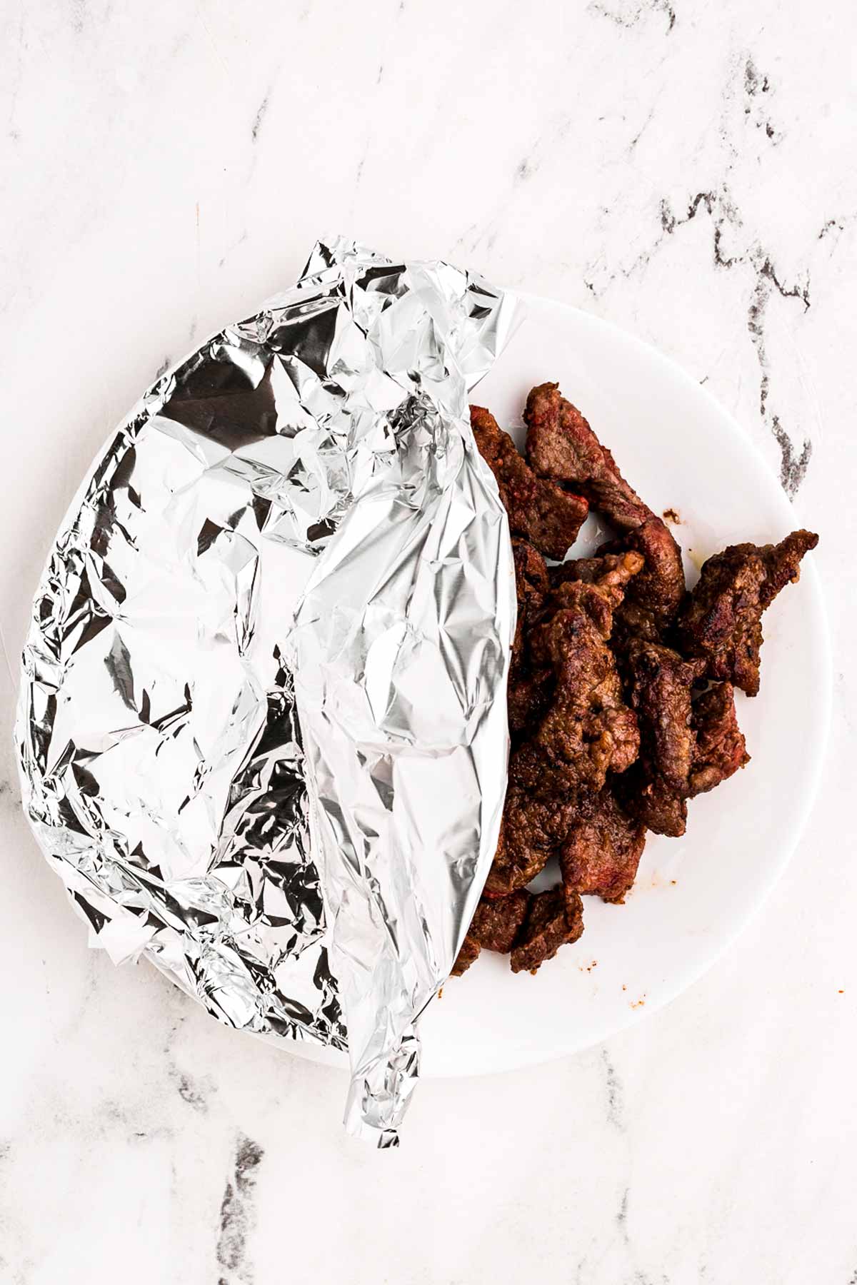 overhead view of seared beef strips tented with foil on plate