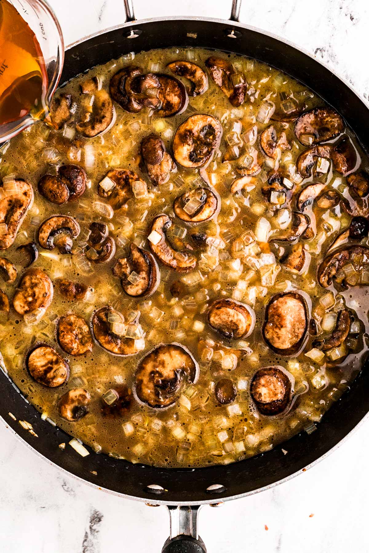 overhead view of beef broth being poured into skillet with mushrooms and onions