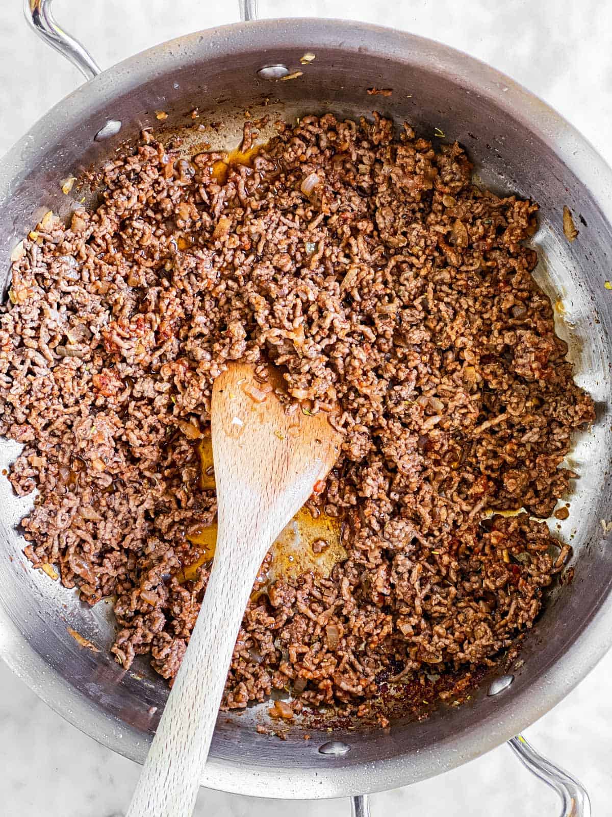 overhead view of browned ground beef in skillet with wooden spoon