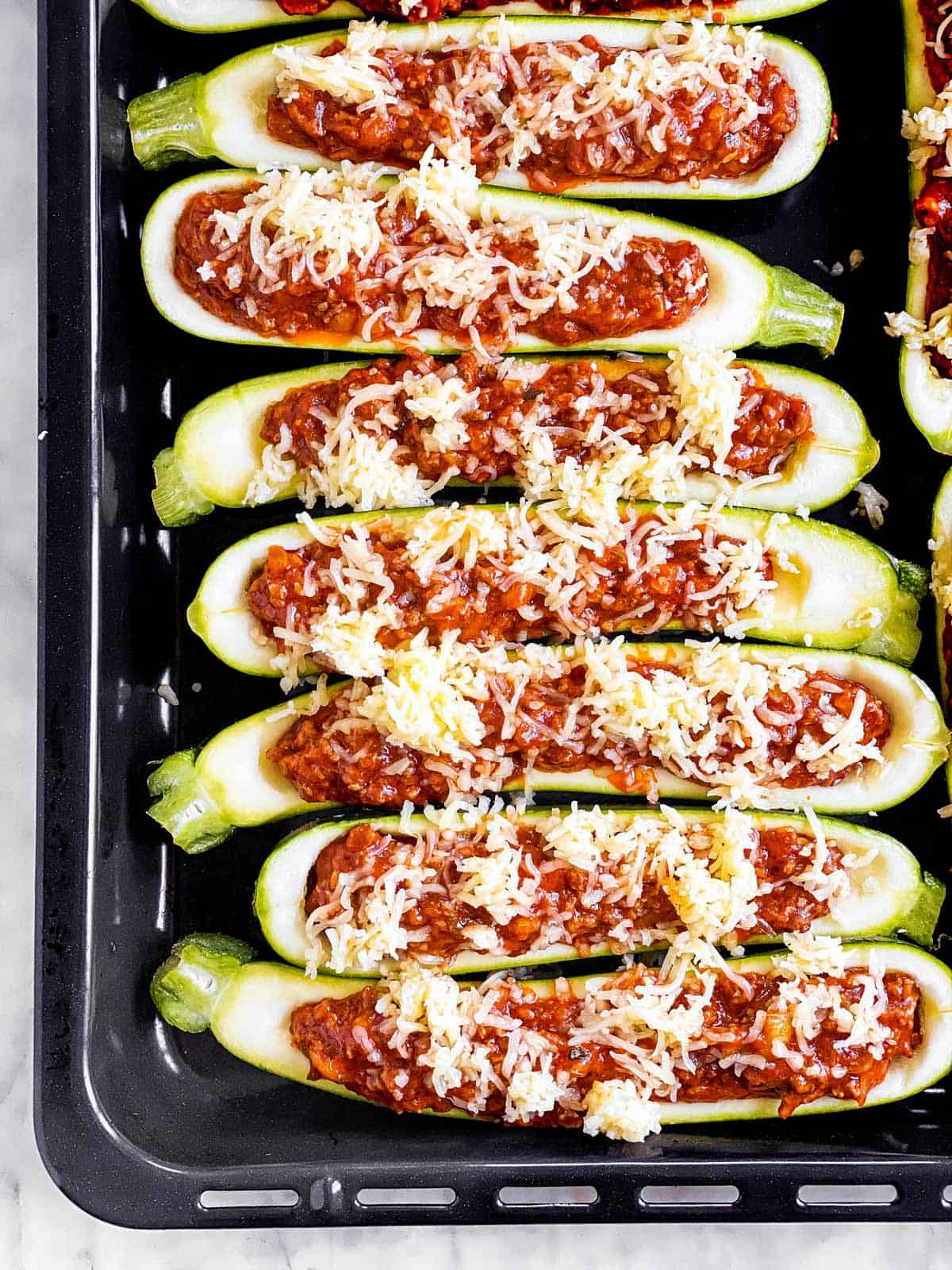 overhead view of unbaked zucchini boats sprinkled with cheese on black sheet pan