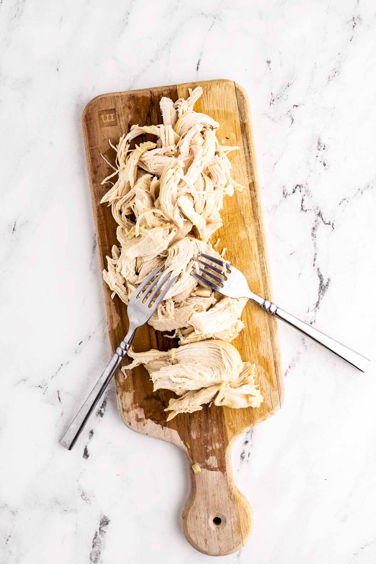 overhead view of shredded chicken on a cutting board with two forks