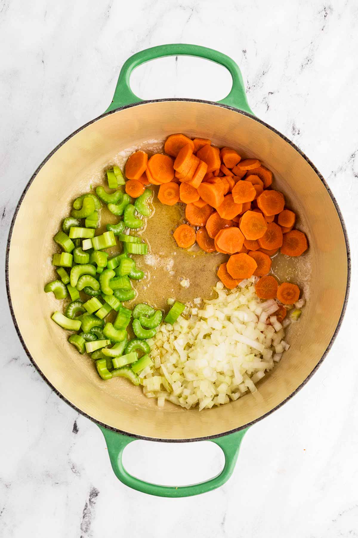 overhead view of uncooked carrots, onion and celery in Dutch oven