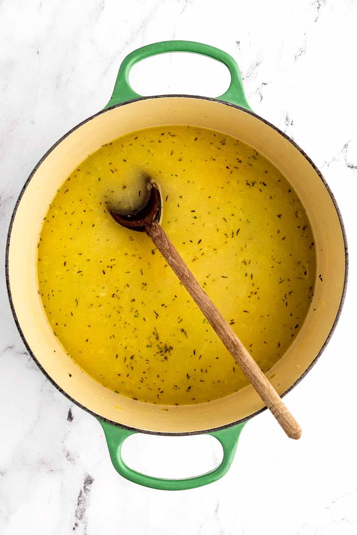 overhead view of broth with wooden spoon in Dutch oven