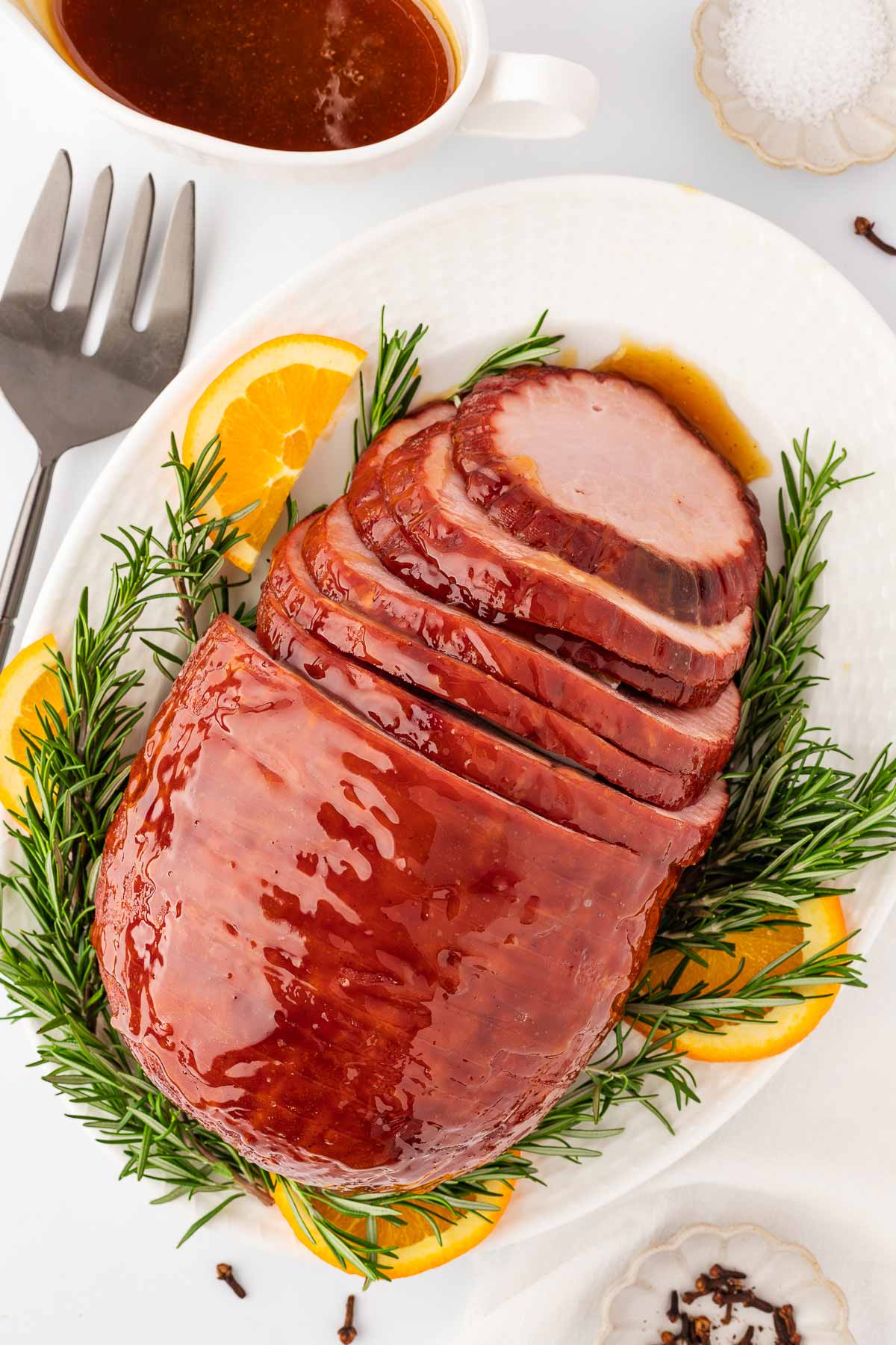 overhead view of sliced honey glazed ham on platter with rosemary and oranges