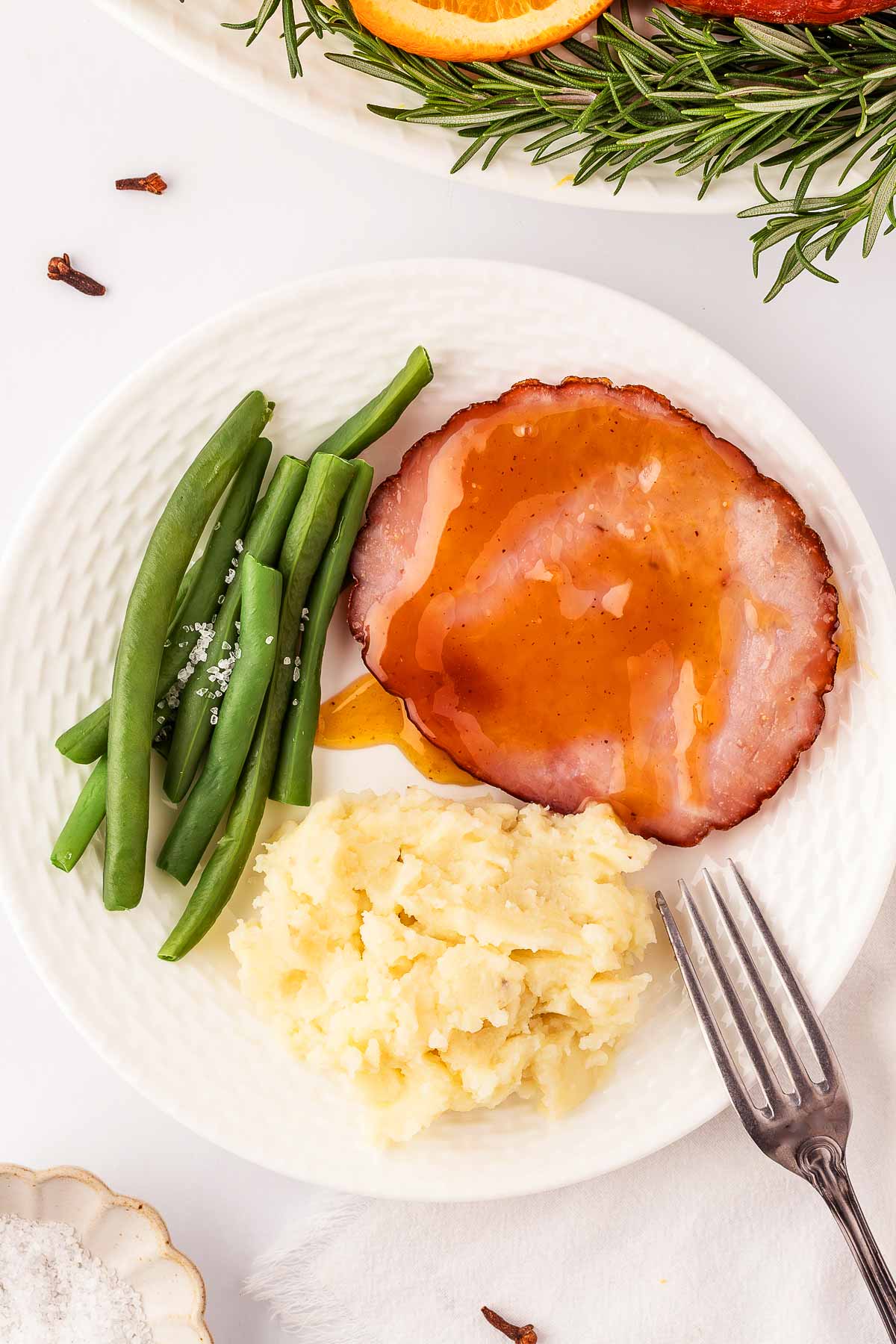 overhead view of glazed ham slices on plate with green beans and mashed potatoes