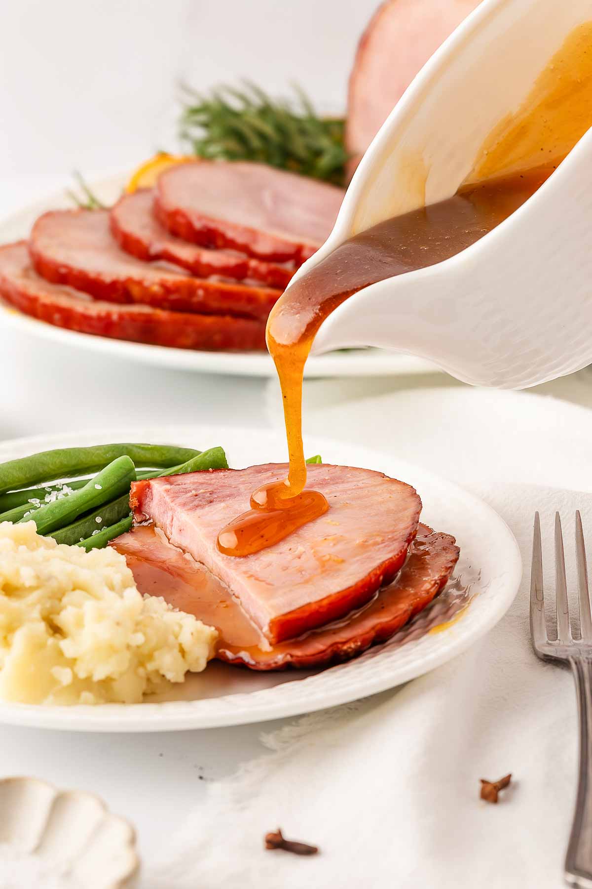 frontal view of honey glaze being drizzled over ham slices on plate