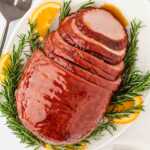 overhead view of sliced honey glazed ham on platter with rosemary and oranges