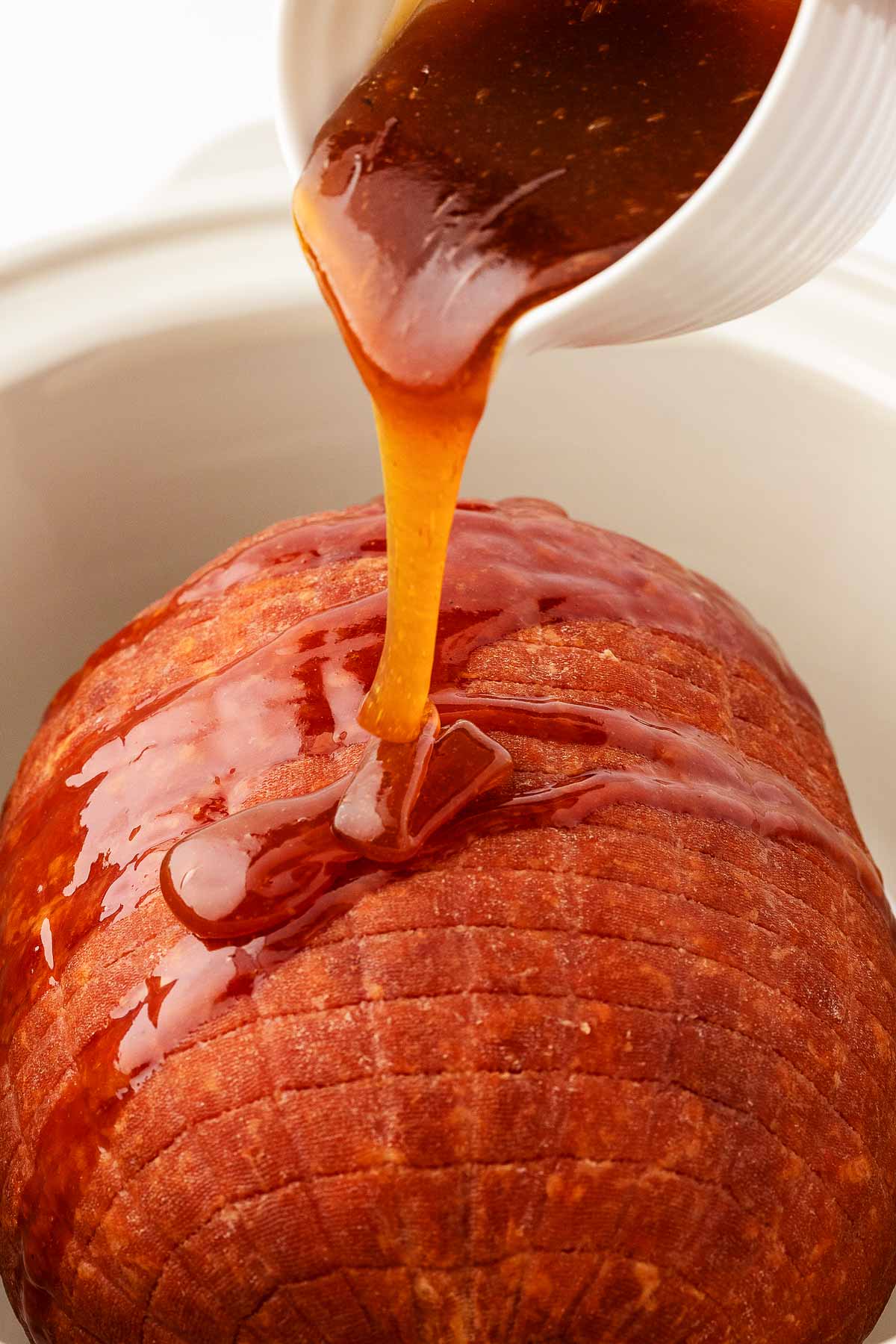 close up view of honey glaze pouring over ham in crock