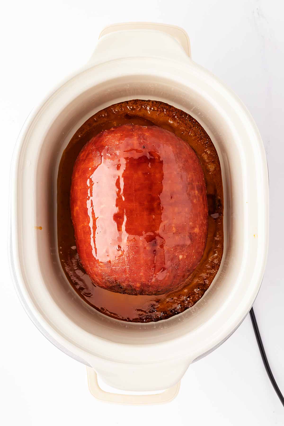 overhead view of cooked glazed ham in white slow cooker