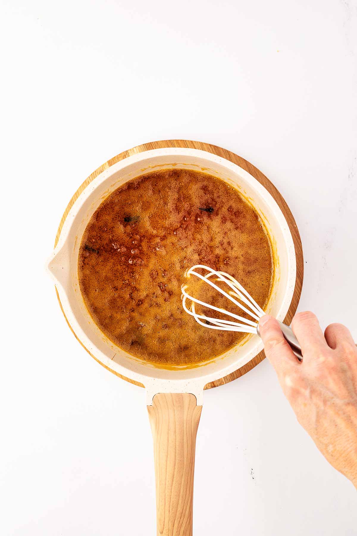 overhead view of female hand whisking honey glaze in white saucepan