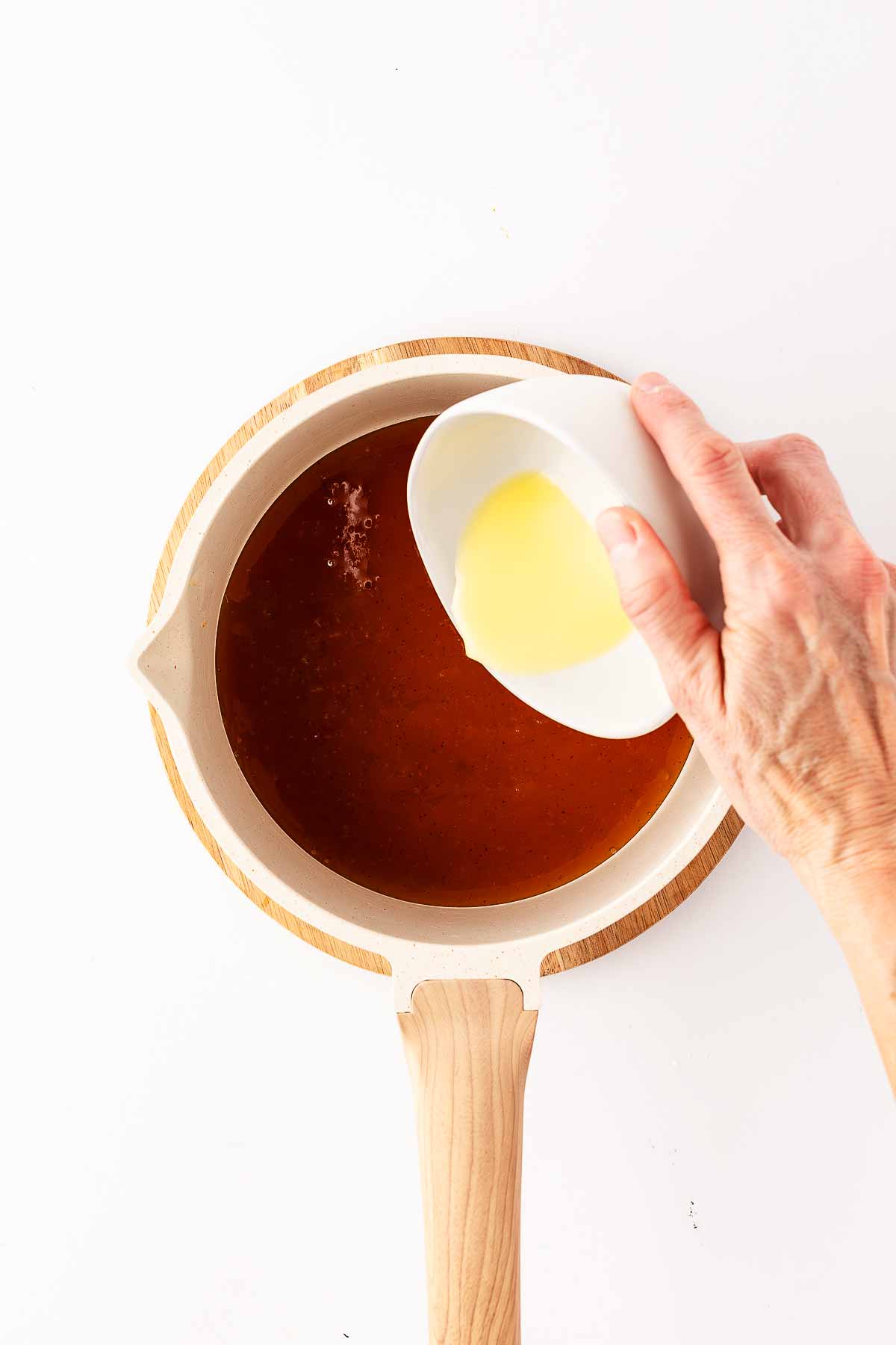 female hand pouring cornstarch slurry into saucepan with ham glaze